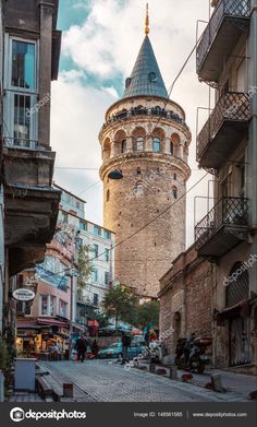 an old stone tower in the middle of a city street with people walking around it