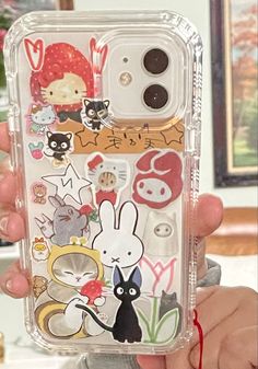 someone is holding up their phone case with stickers on it and there are many other things in the back