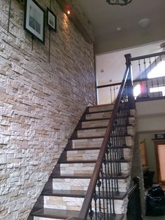 a stair case next to a stone wall and wooden handrail in a living room