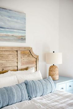 a bed with white sheets and blue pillows in a bedroom next to a painting on the wall