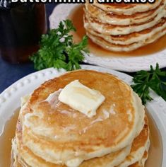 stack of pancakes with butter and parsley on top sitting on a white plate next to a bottle of syrup