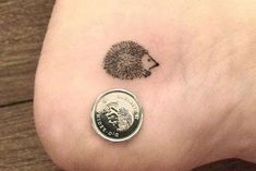 a small hedgehog tattoo on the ankle with a penny in it's left foot