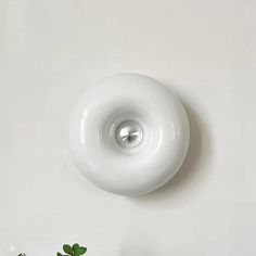 a white light fixture mounted on the side of a wall next to a potted plant