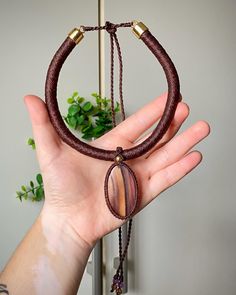 a hand holding a brown bracelet with two beads on it and a green plant in the background