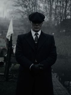 a man in a suit and tie standing next to a body of water on a foggy day