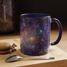 a purple coffee mug sitting on top of a wooden cutting board next to a spoon