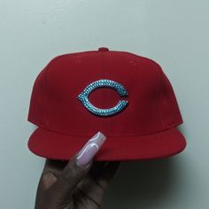 a person holding up a red baseball cap with the letter c embroidered on it's side