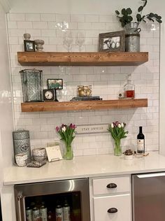 a kitchen with two open shelves above the sink and some flowers in vases on the counter