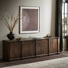 a living room with a large painting on the wall next to a wooden sideboard