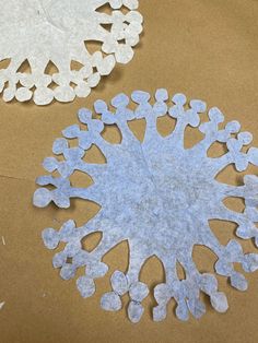 two paper snowflakes sitting on top of a brown table next to each other