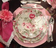 a table set for two with pink flowers and silverware on it, along with utensils