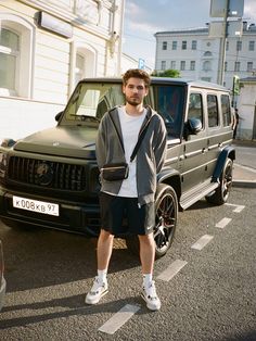 a man standing in front of a black mercedes benz g - class parked on the street