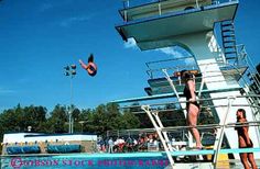 two people diving off the side of a boat in an open swimming pool while others watch