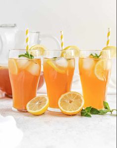 three glasses filled with orange juice and lemon slices next to each other on a table