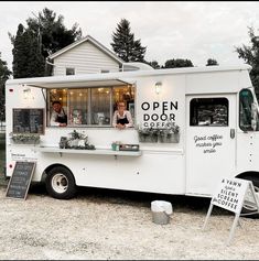 an open door coffee truck is parked in front of a sign and some trees outside