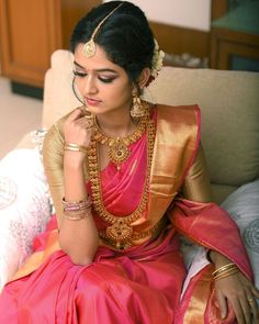 a woman in a pink and gold sari sitting on a couch with her hands to her face