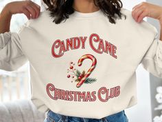 a woman wearing a candy cane christmas club sweatshirt in front of a white couch with the words candy cane on it