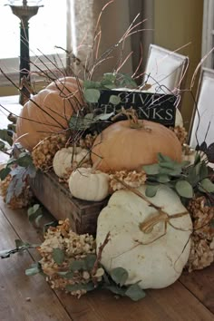 an arrangement of pumpkins and gourds in a wooden crate on a table