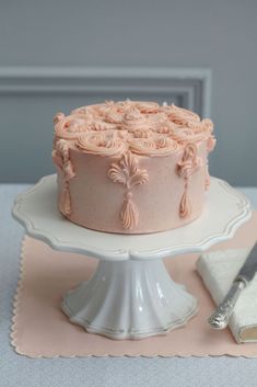 a pink cake sitting on top of a white plate next to a knife and fork