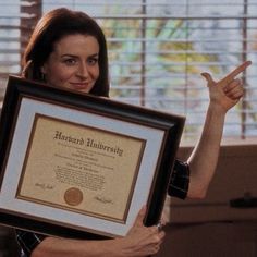 a woman holding up a framed award in front of her face and pointing to the side