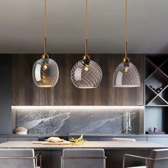 three glass pendant lights hang over a kitchen island with marble counter tops and chairs in front of it