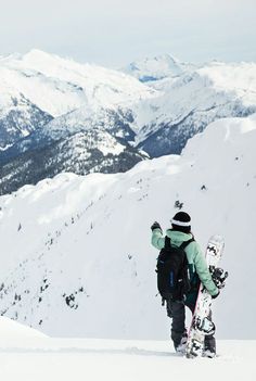 a snowboarder is walking up the side of a mountain with mountains in the background