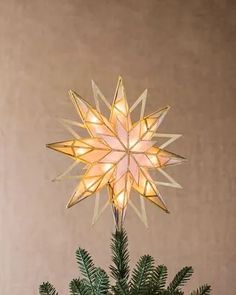 a lighted star on top of a small christmas tree with pine branches in the foreground