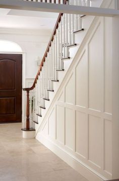 an open door leading to a hallway with white walls and wooden stairs in the background