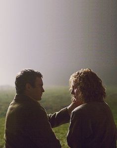 two people sitting on a bench looking at each other with fog in the sky behind them