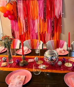 the table is set for a party with pink plates and red napkins on it