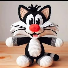 a crocheted black and white cat sitting on top of a wooden table next to a red nose