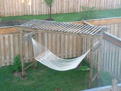 a hammock hanging from a wooden structure in a yard with grass and fence