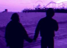 two people holding hands while standing in front of a ferris wheel at dusk on the beach