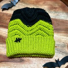 a green and black knitted hat sitting on top of a wooden table next to a bat