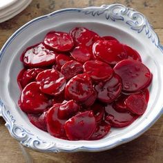 a bowl filled with sliced up beets sitting on top of a wooden table next to silverware