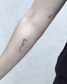 a woman's arm with a tiny seahorse tattoo on it