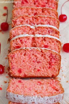 several slices of cake sitting on top of a cutting board next to some cherries