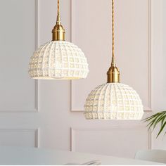 two white lamps hanging from a ceiling in a room with a potted plant on the table