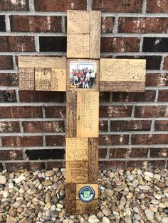 a wooden cross sitting on top of a pile of rocks next to a brick wall