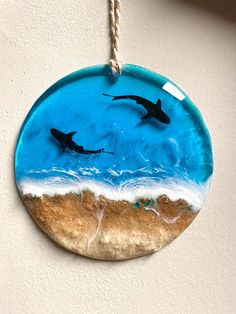 two dolphins swimming in the ocean on a beach glass ornament hanging from a rope