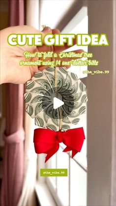 someone holding up a dollar bill ornament with a red bow on it's end