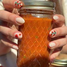 a woman holding a jar filled with food and wearing nail art on her nails,