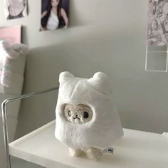 a white teddy bear sitting on top of a table next to a wall with pictures