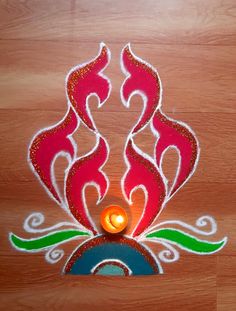 a decorated diya with a lit candle in the center on a wooden surface,