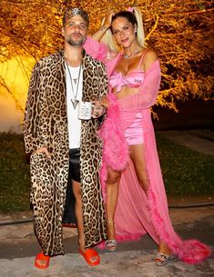 a man and woman dressed up in animal print outfits standing next to each other at night