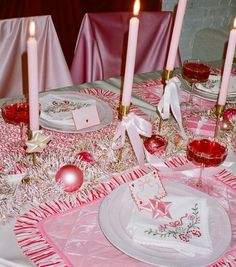 the table is set for christmas dinner with pink and white decorations, candles, and napkins