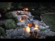 a garden with rocks and water features lights on each side, along with plants and shrubs