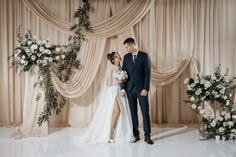 a bride and groom standing next to each other in front of a wedding arch with flowers