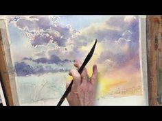 a person holding a pair of scissors in front of a painting with clouds on it