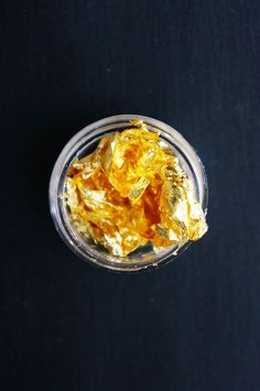 a glass bowl filled with gold flakes sitting on top of a table next to a black surface